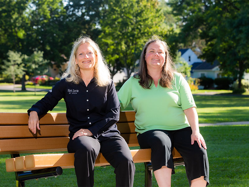 MGE energy experts, Laura Paprocki and Leah Samson, sitting on a bench at a park.