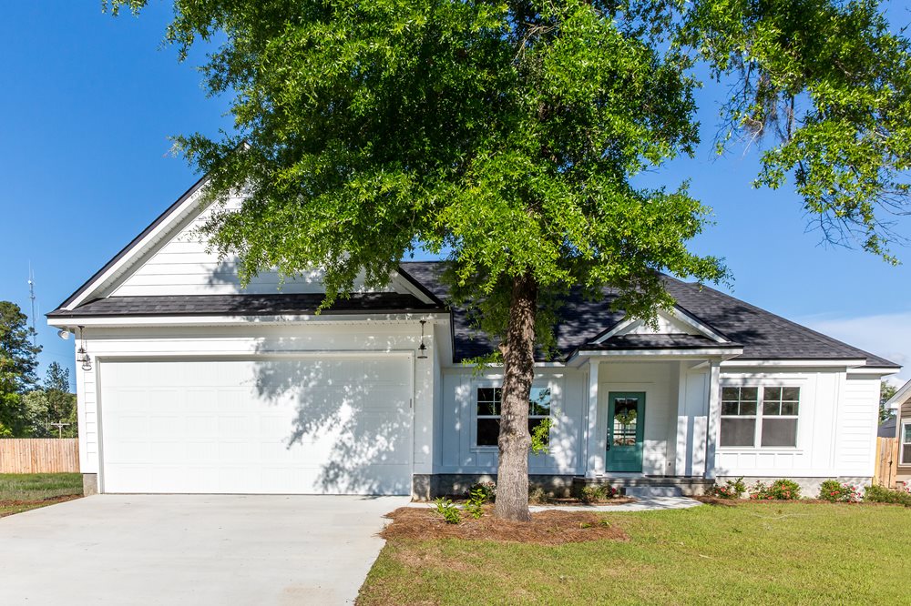 A white two-story house shaded by a leafy green tree.