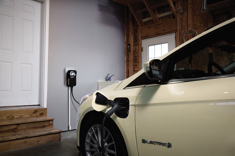 A closeup of a white, electric Ford Focus plugged in and charging in the garage.